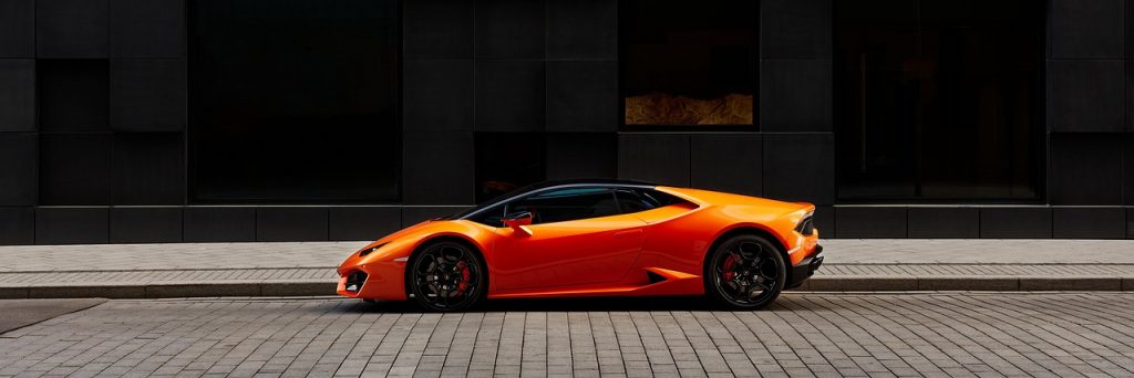 bright orange Lamborghini Huracán parked on a clean, modern cobblestone street.