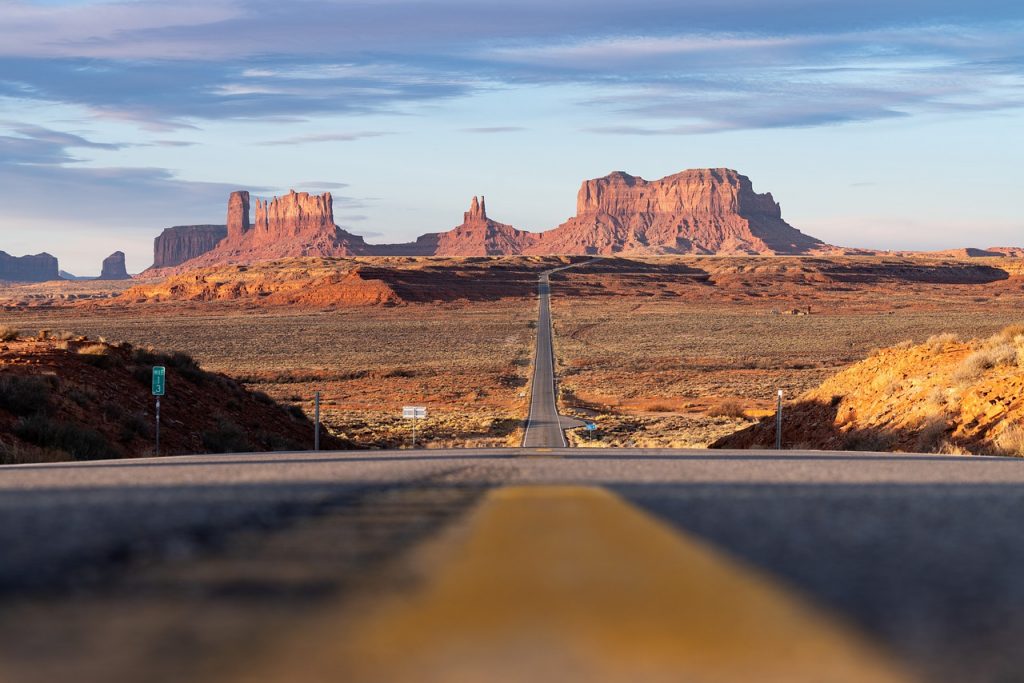 Low-angle view of a straight desert highway leading into Monument Valley, symbolizing freedom with Montana vehicle registration.