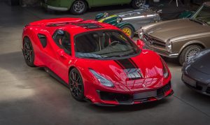 A striking red sports car with black racing stripes sits among classic and exotic vehicles, symbolizing the peace of mind that comes from registering your car the right way.