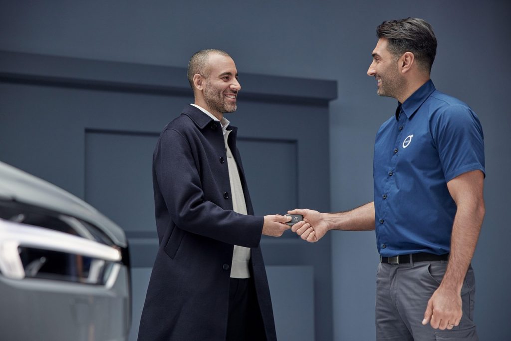A smiling customer receives a car key from a dealership employee, symbolizing the completion of a successful vehicle transaction.