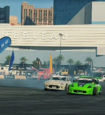 Two modified sports cars drift side by side in a smoky, high-speed performance at an outdoor auto event in Las Vegas.